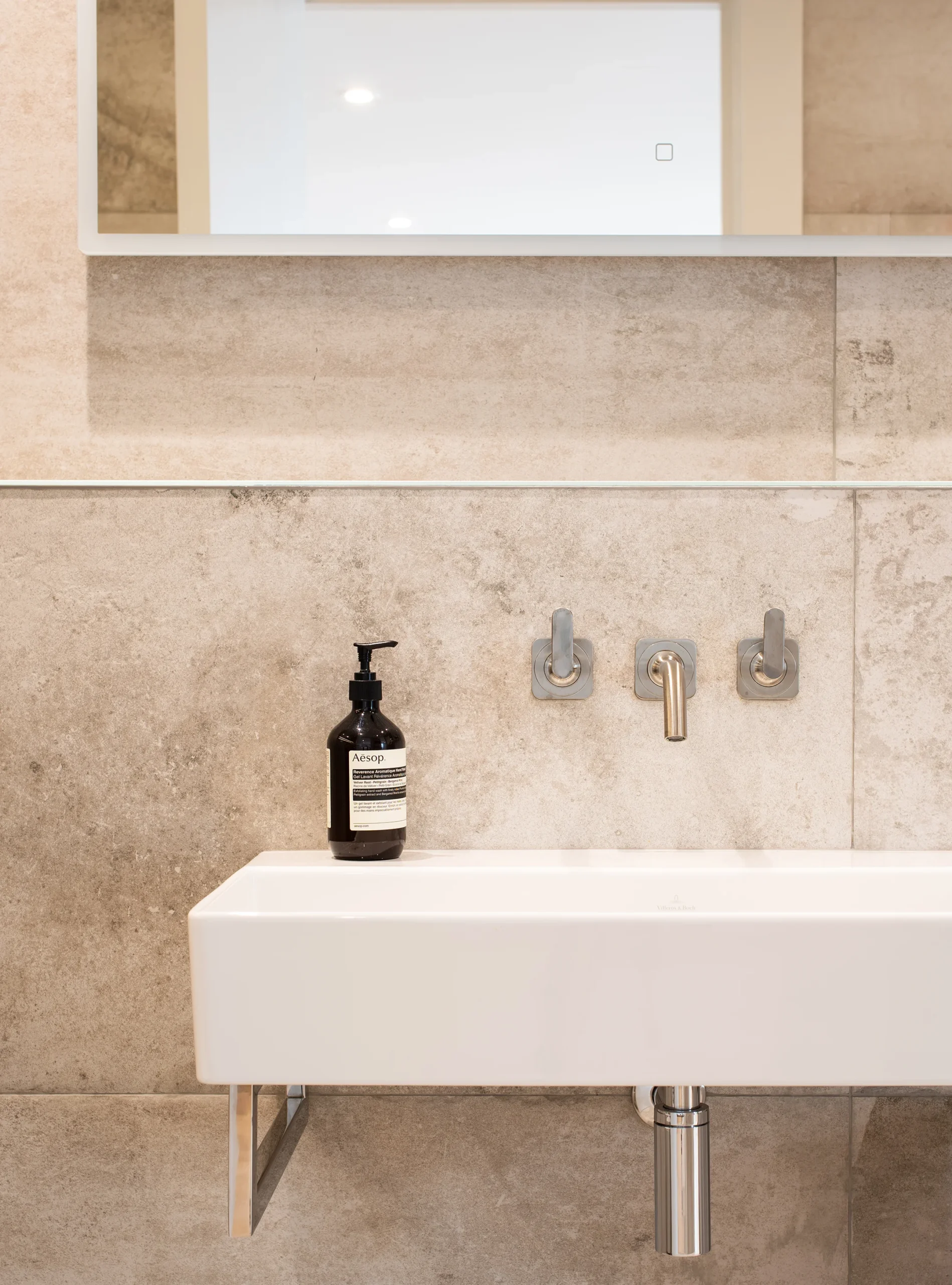 Wall-hung stone basin with wall-mounted brushed nickel taps and stone tiled walls