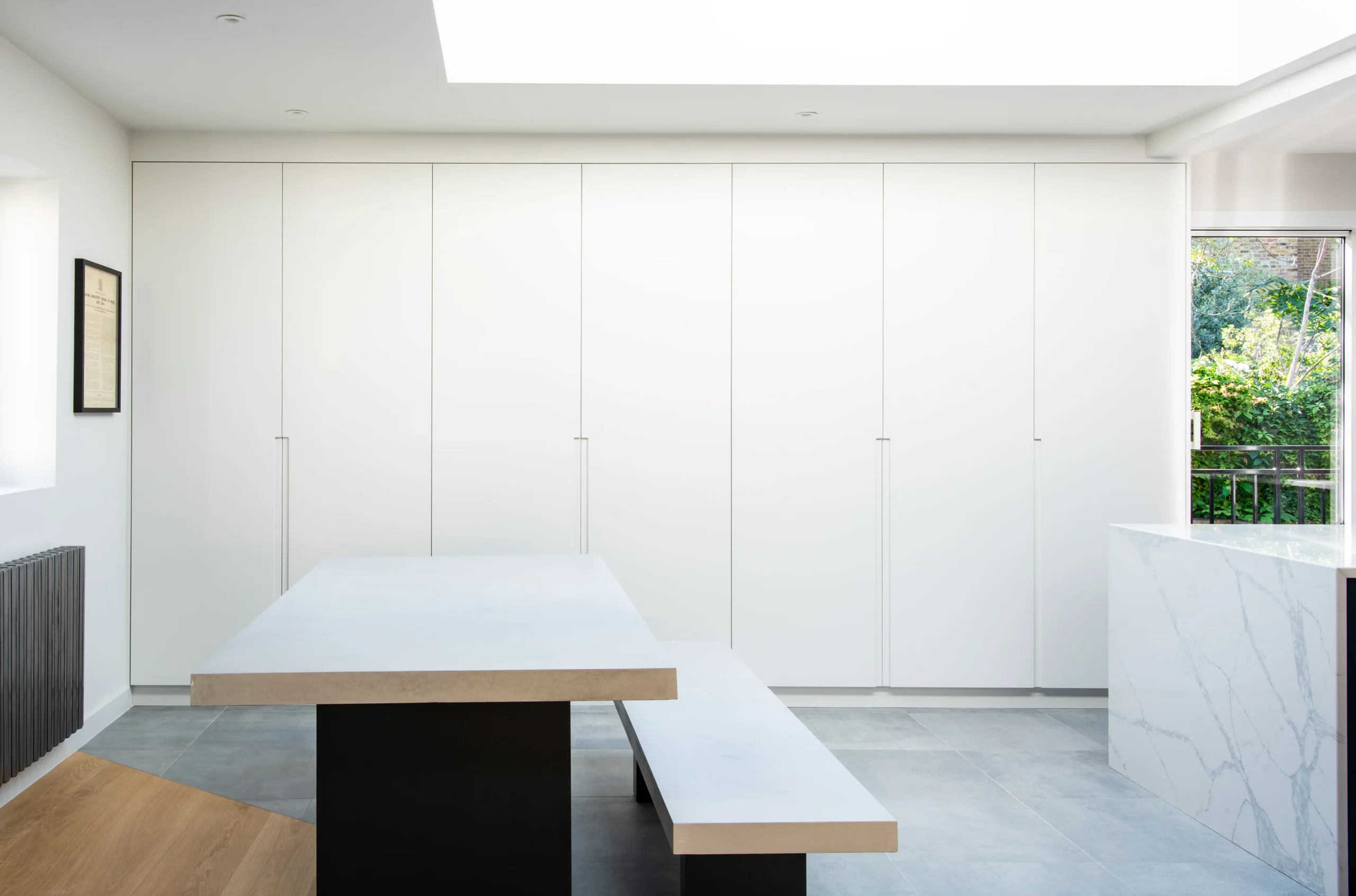 Dining area with a full-height handleless white joinery wall, bench seating and marble island