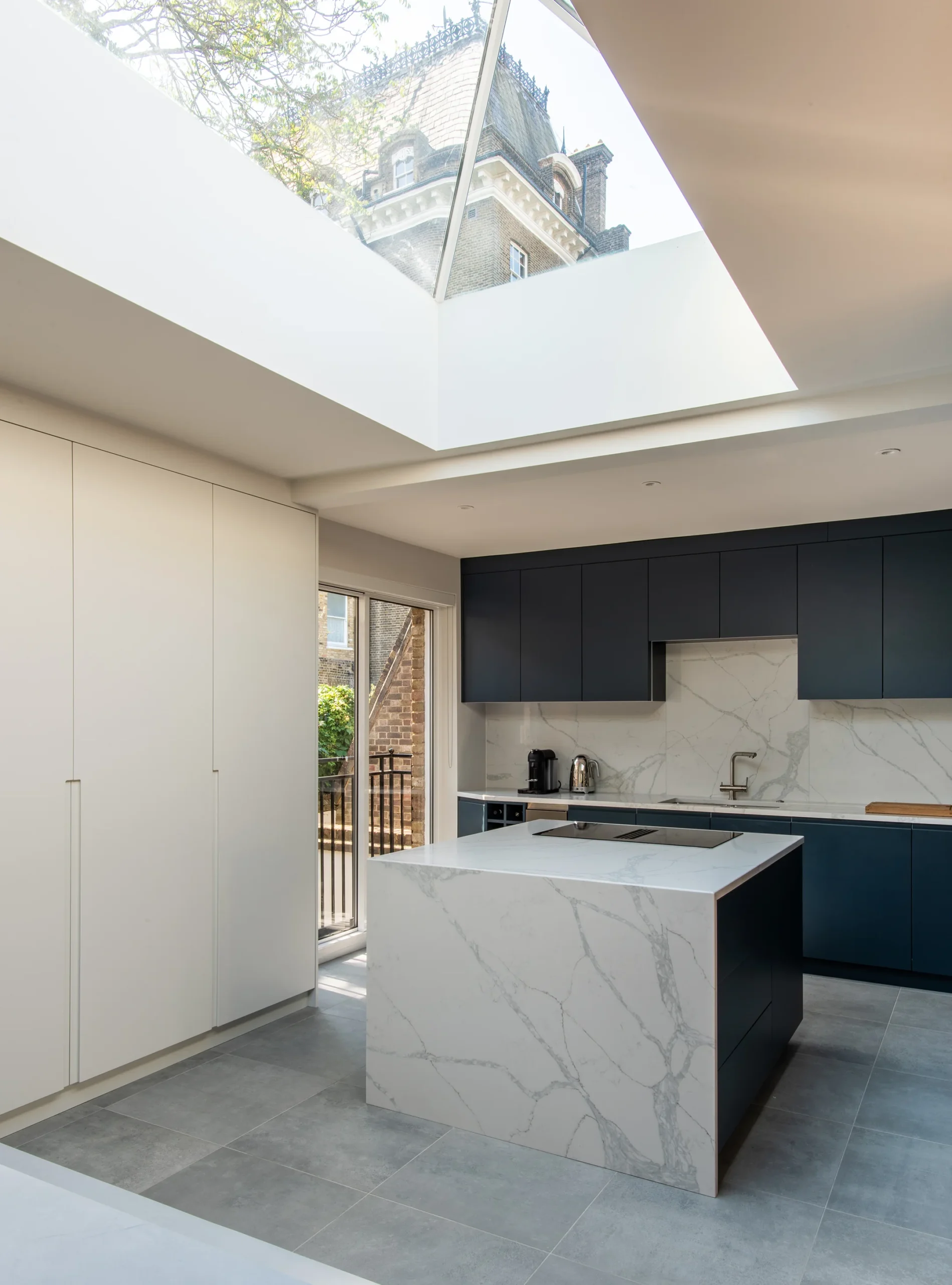 Kitchen and dining space under a rooflight with flush white joinery, navy units and marble island