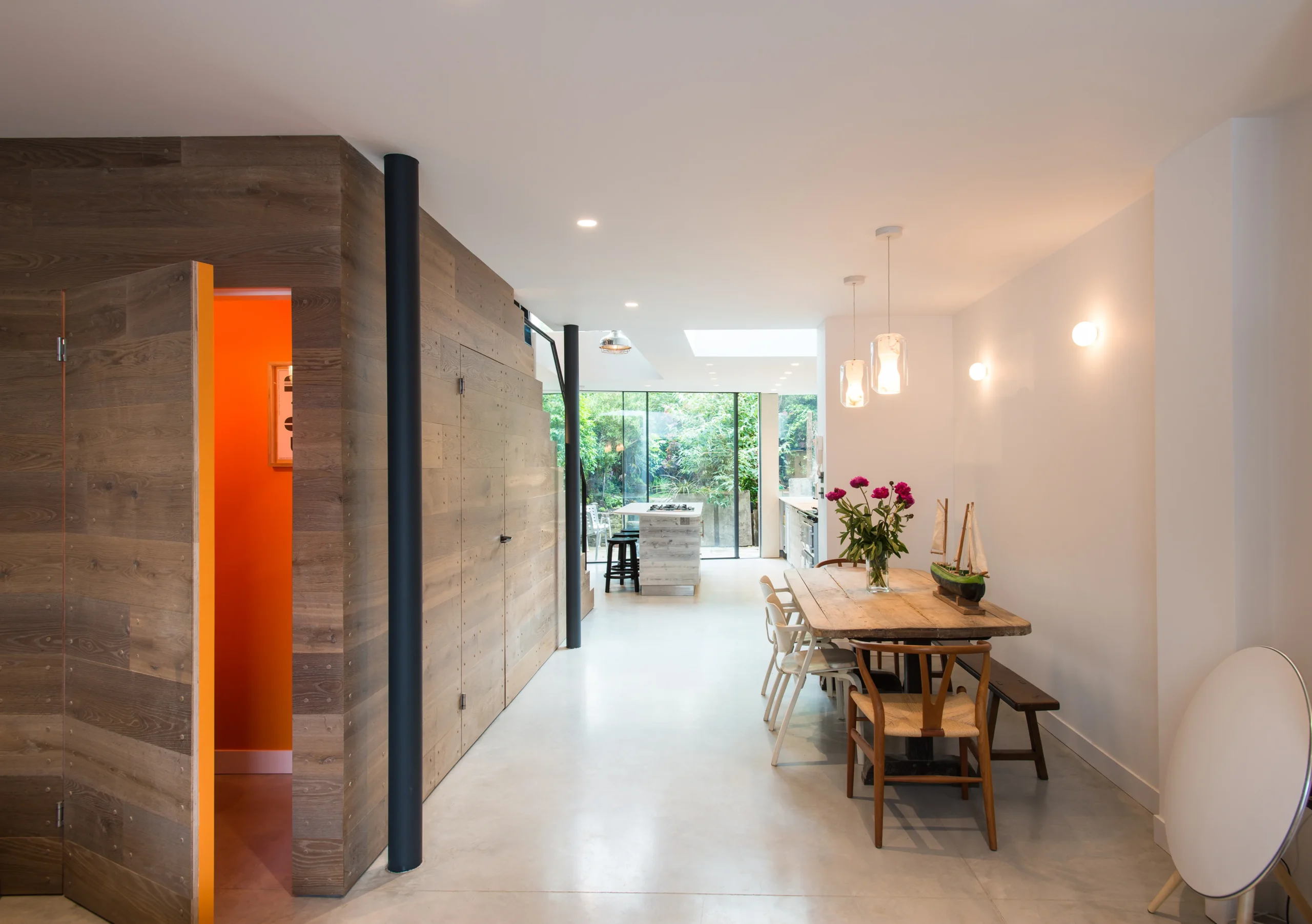 Camden_11_3840px Reclaimed timber-clad wall with a flush door opening onto an orange room, dining area and garden beyond