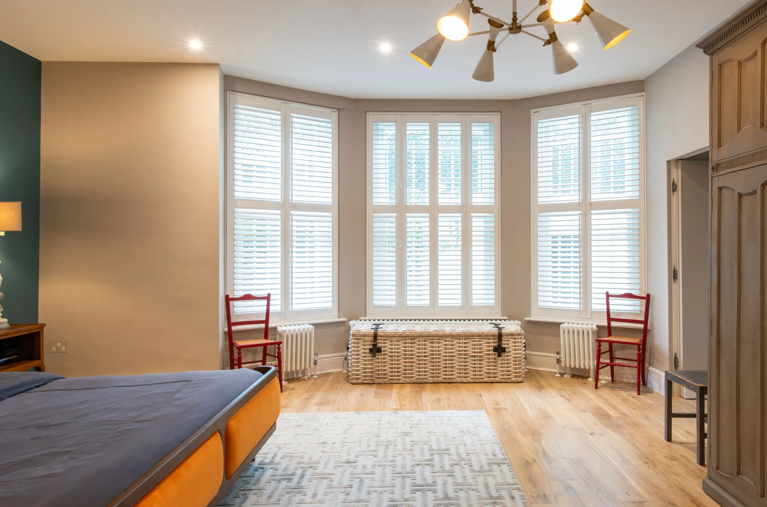 Basement bedroom with shuttered bay window, oak floor and sunburst ceiling light
