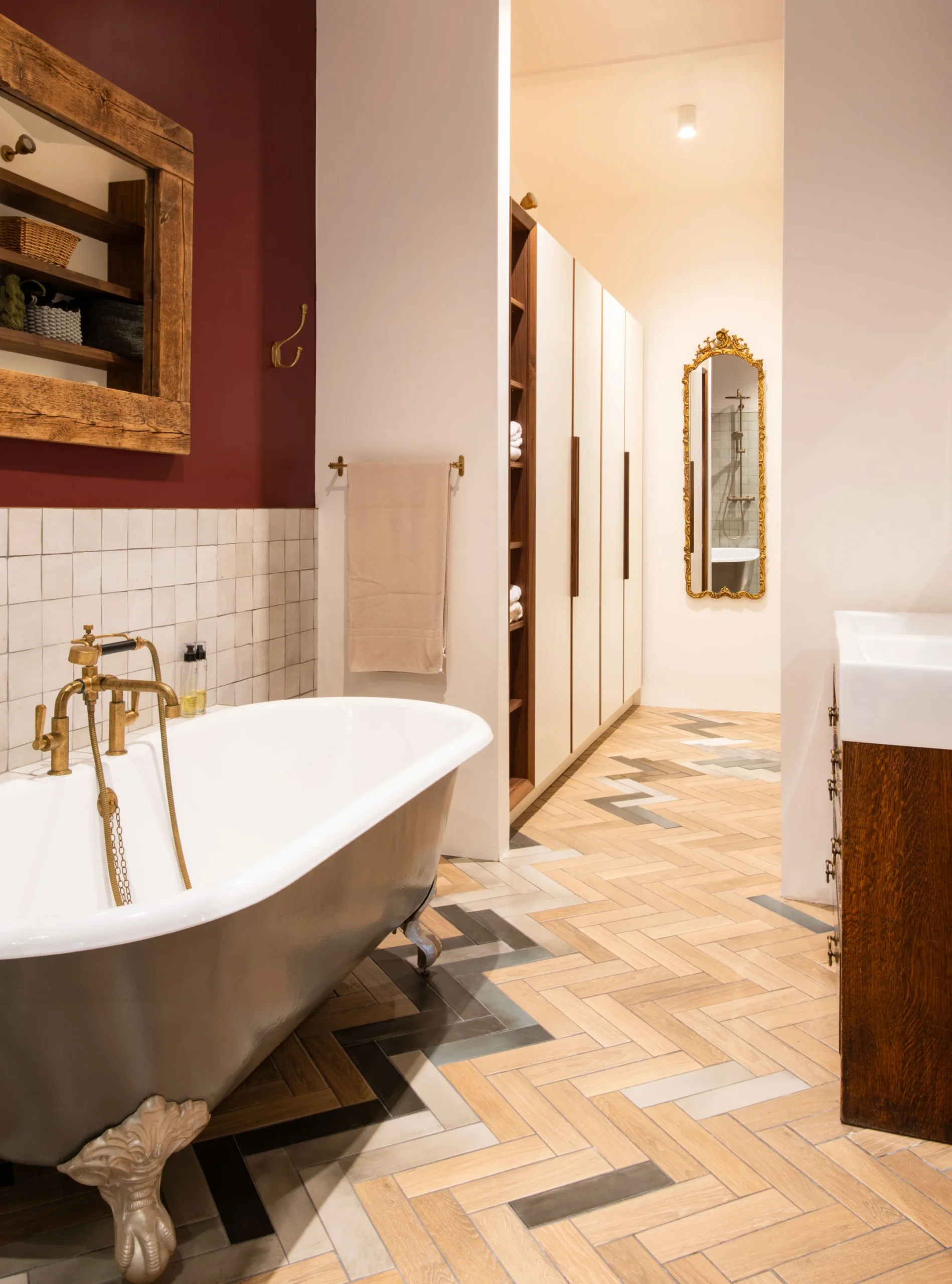 Bathroom with claw-foot roll-top bath, brass fittings, deep red wall and herringbone floor tiles