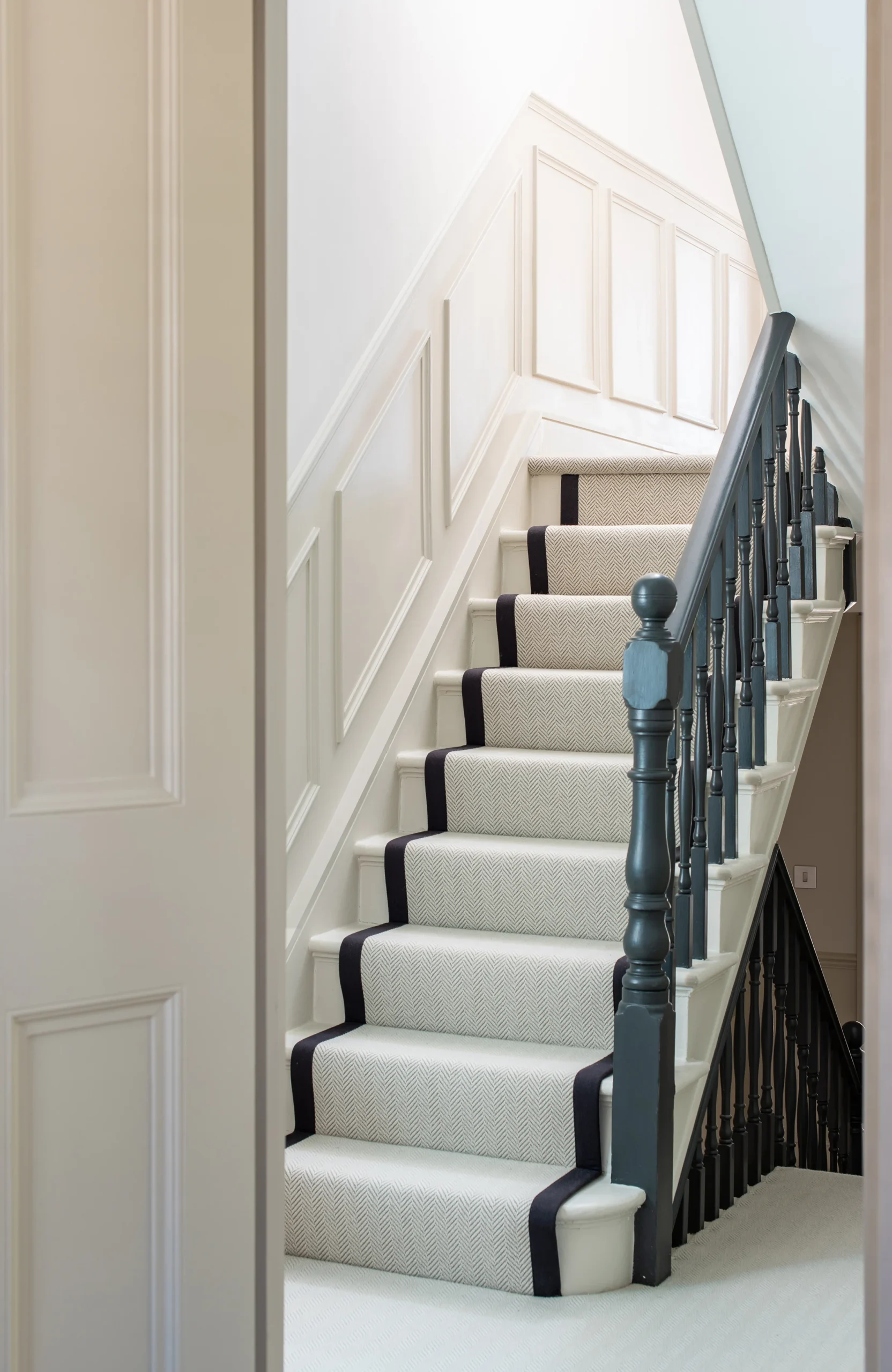 Staircase with grey runner, panelled wall and dark painted balustrade