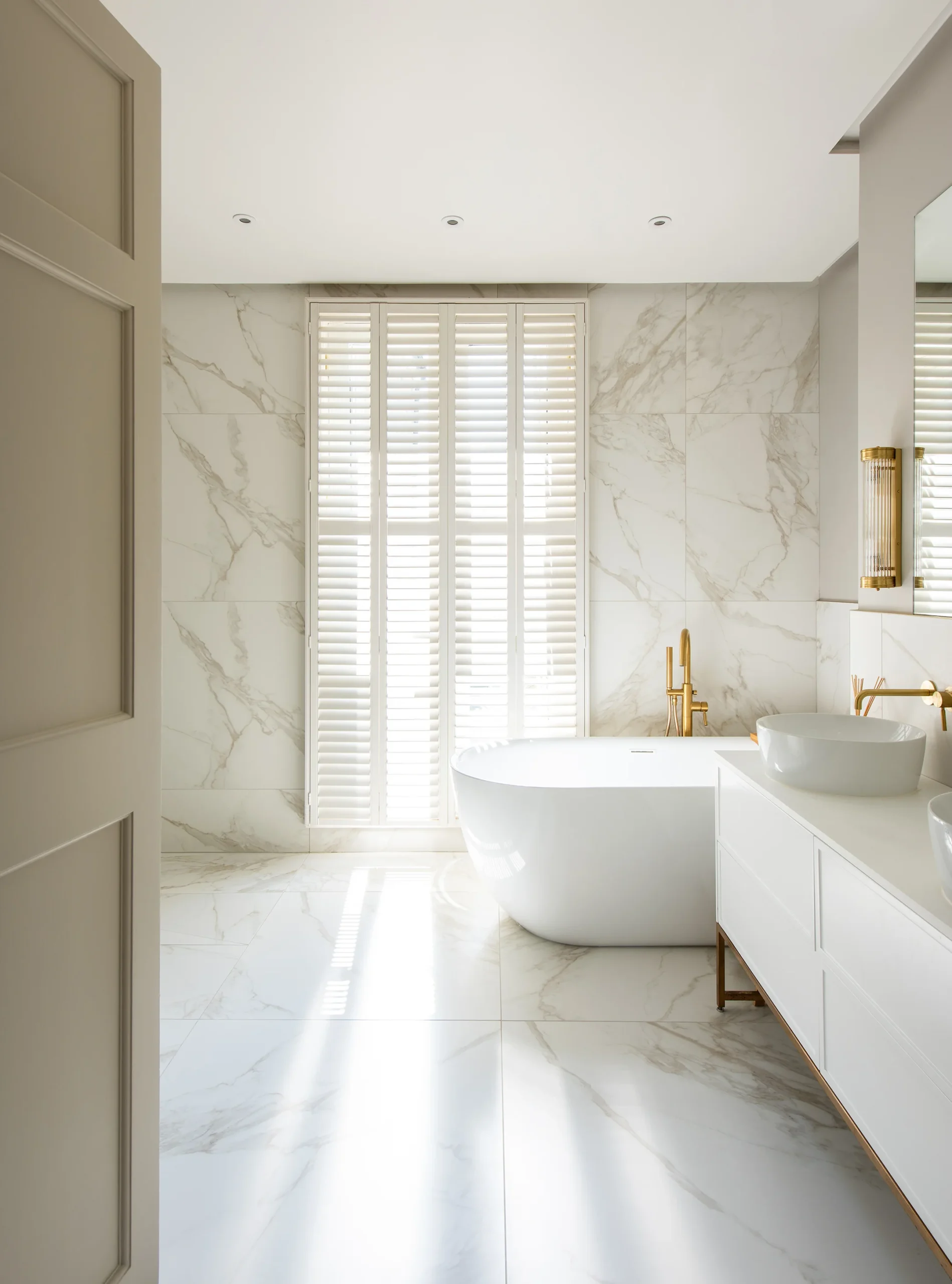 Bathroom with freestanding bath, marble-effect tiles and plantation shutters