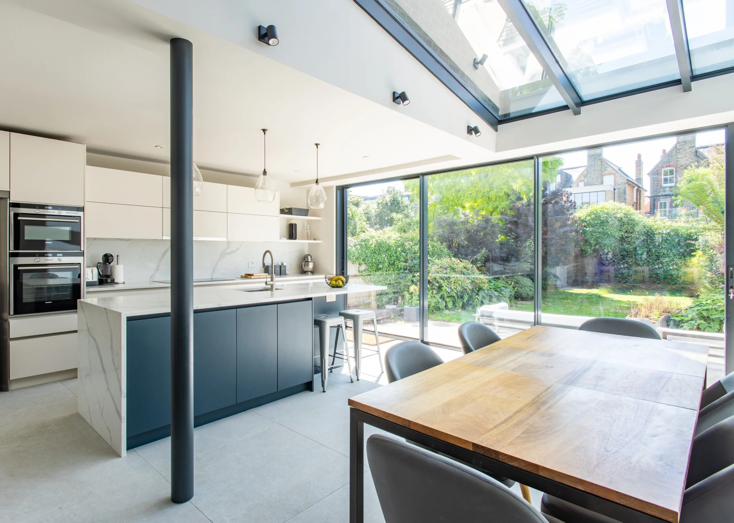 Side return kitchen extension under a pitched glass roof, with navy island and dining table