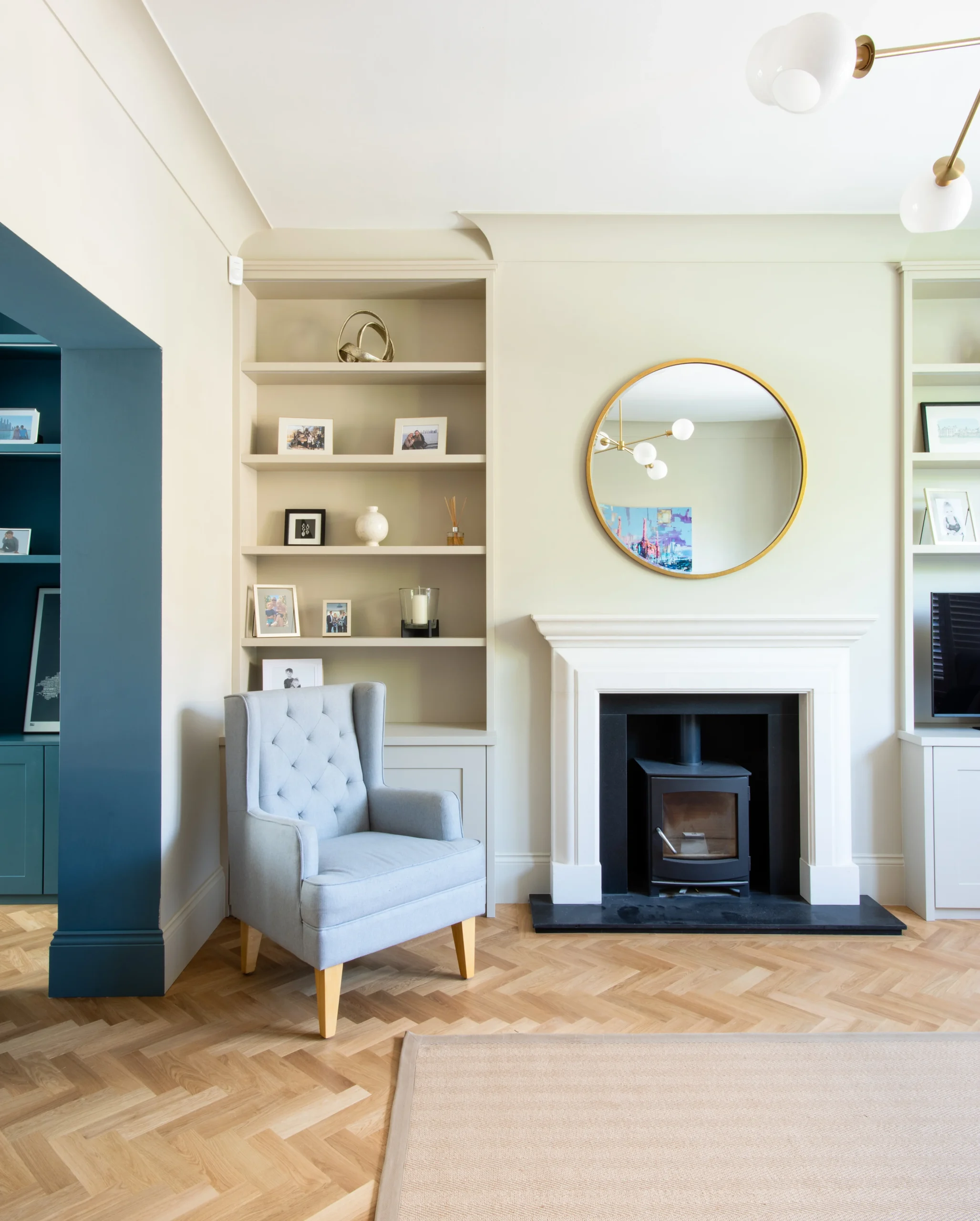 Sitting room with herringbone parquet, fitted alcove shelving, round mirror and wood burner