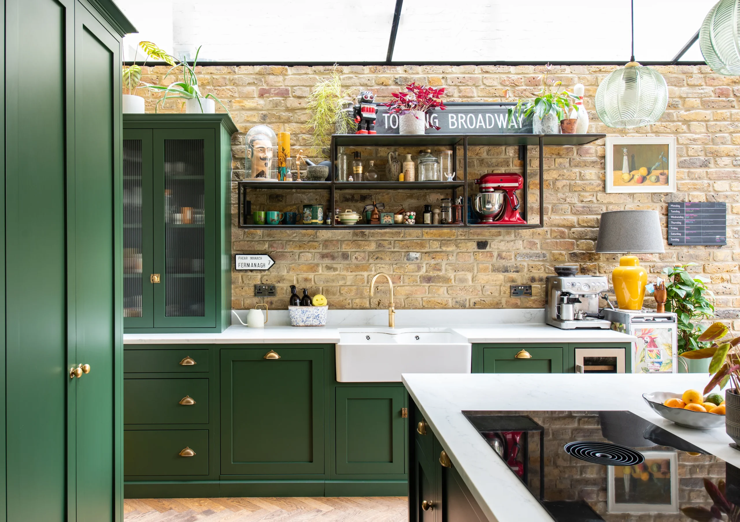 Green in-frame shaker kitchen with brass cup handles, butler sink and black steel shelving on exposed London stock brick
