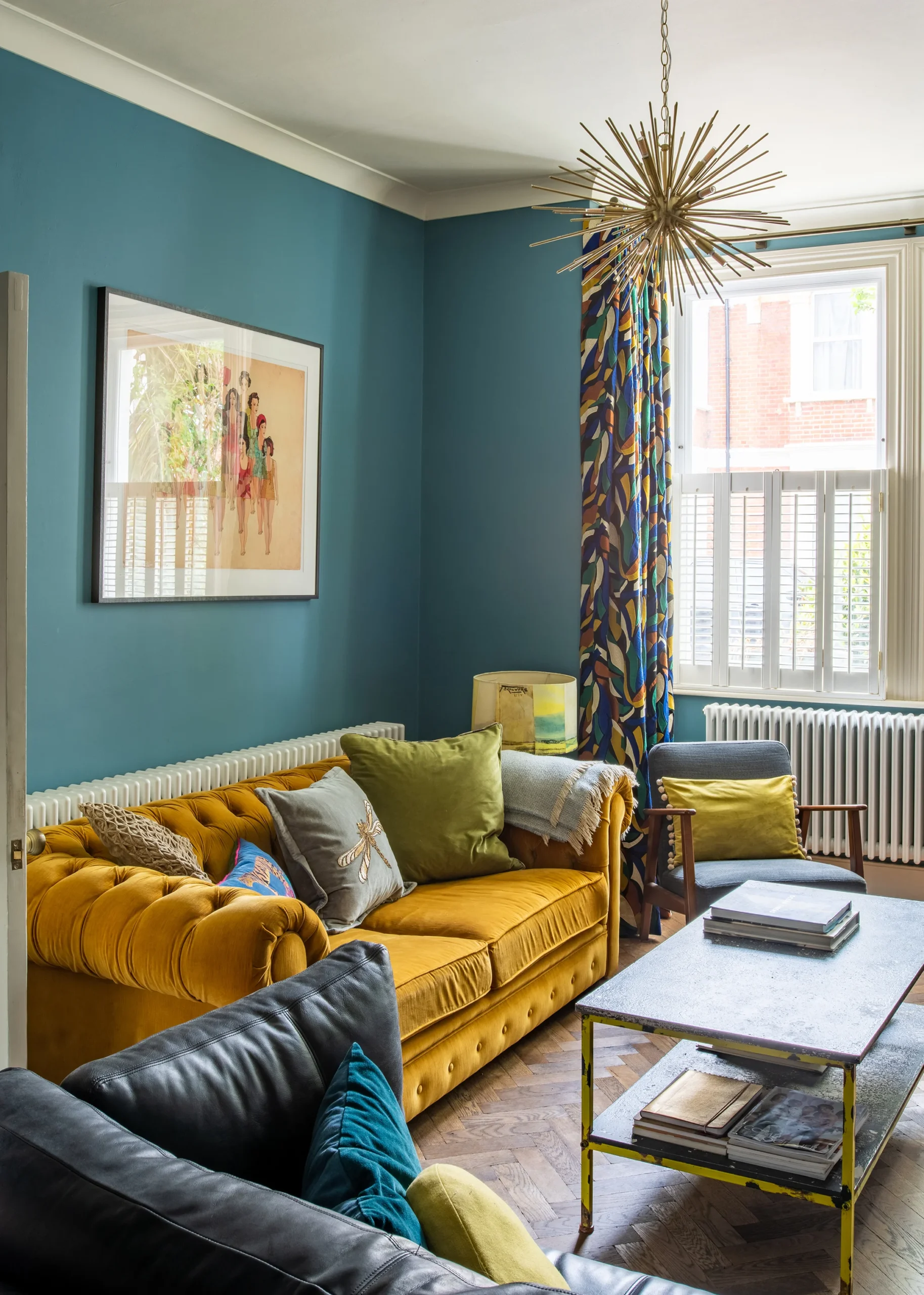 Sitting room with teal walls, mustard velvet sofa and shuttered bay window