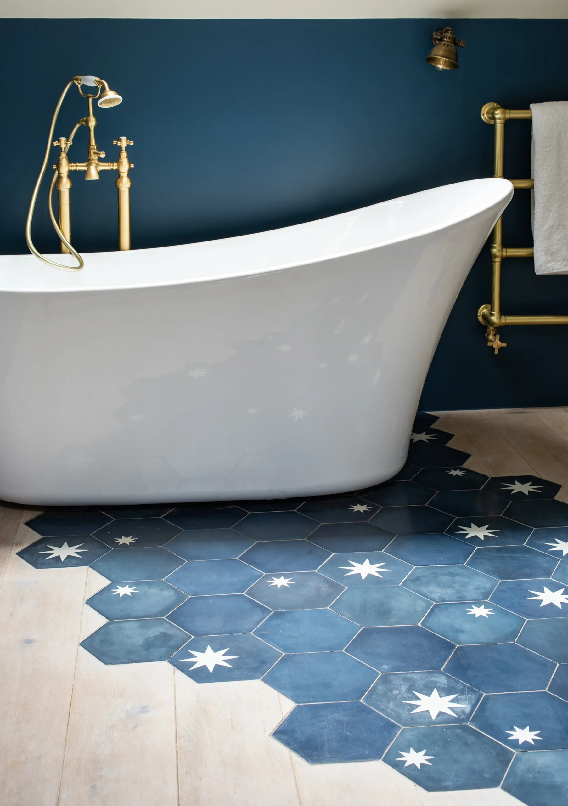 Freestanding slipper bath against a deep blue wall over blue hexagonal tiles with white star inlay