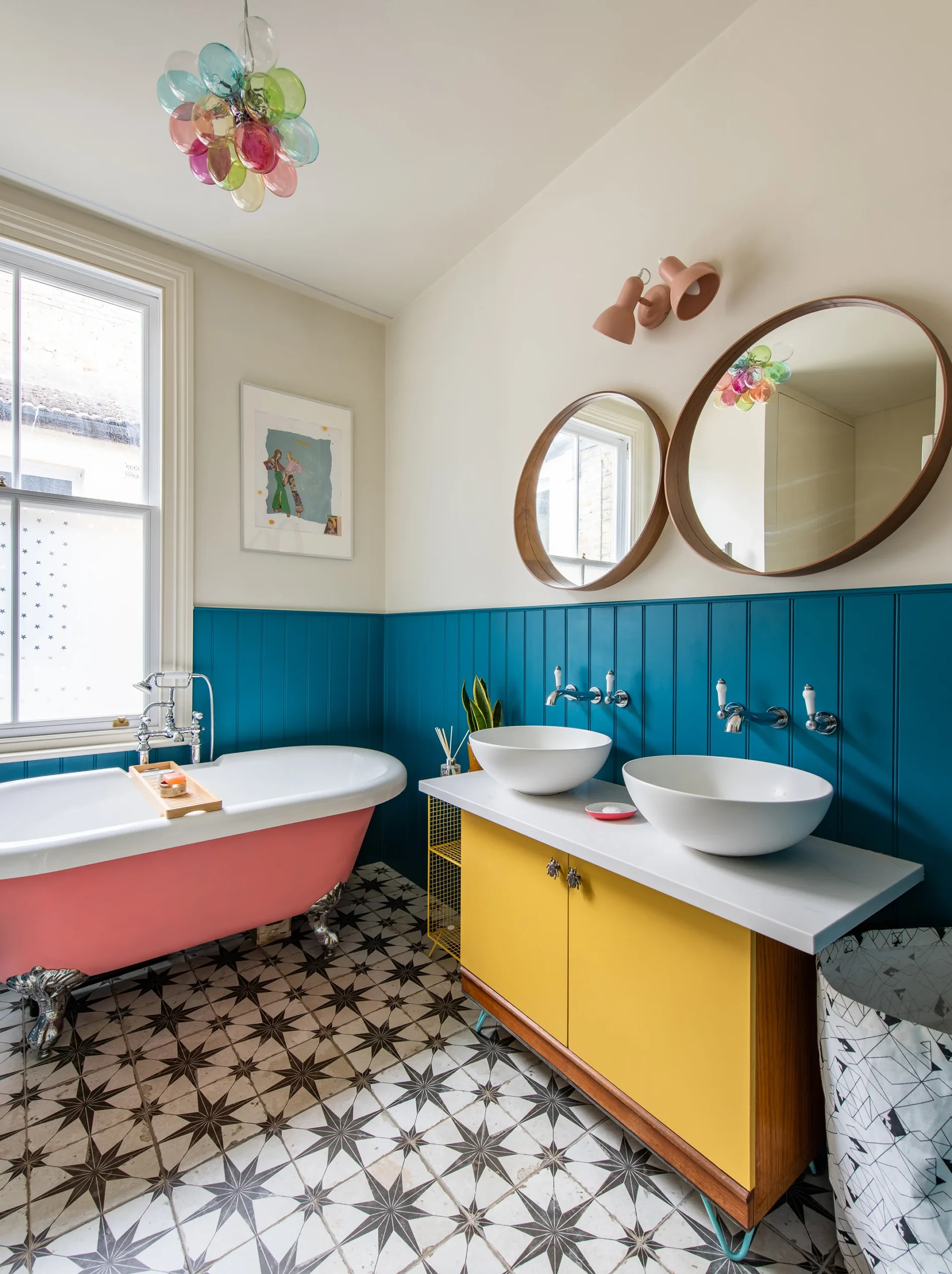 Family bathroom with pink roll-top bath, blue panelling, yellow double vanity and patterned floor tiles