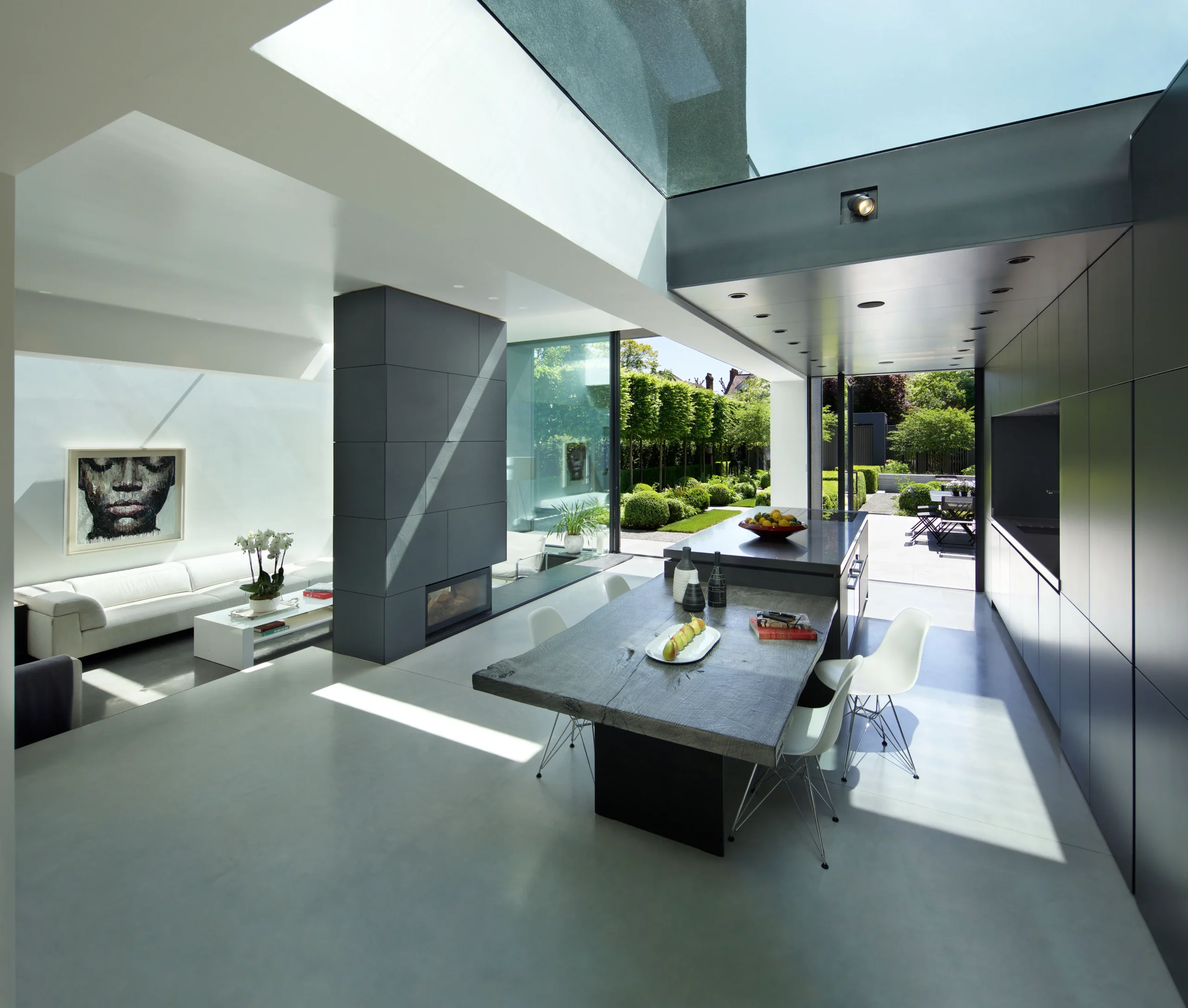 Open-plan kitchen and dining space with structural glazing, polished concrete floor and dark full-height joinery