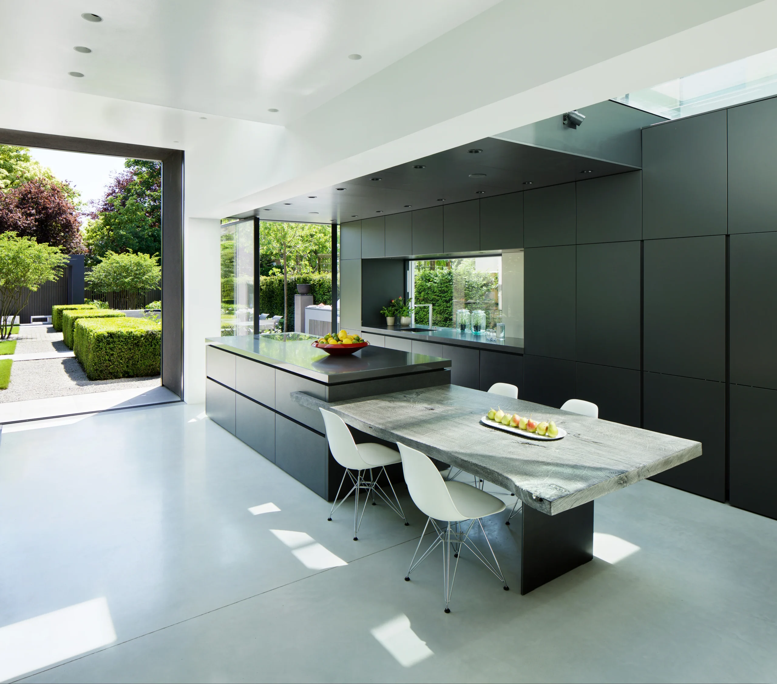 Kitchen extension in Ealing with dark full-height cabinetry, stone island and glazed wall opening onto the garden