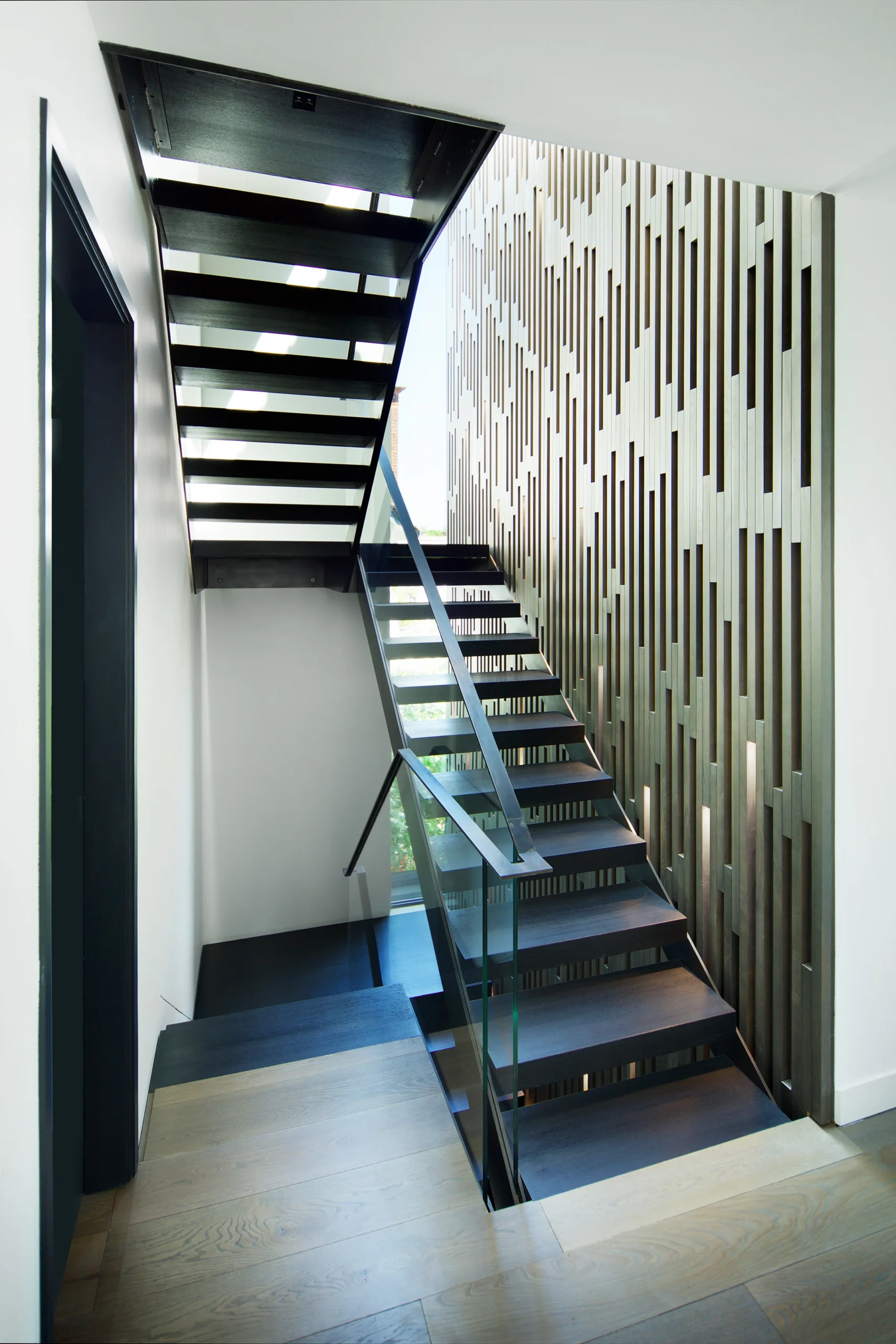 Steel and glass staircase rising beside a slatted timber wall