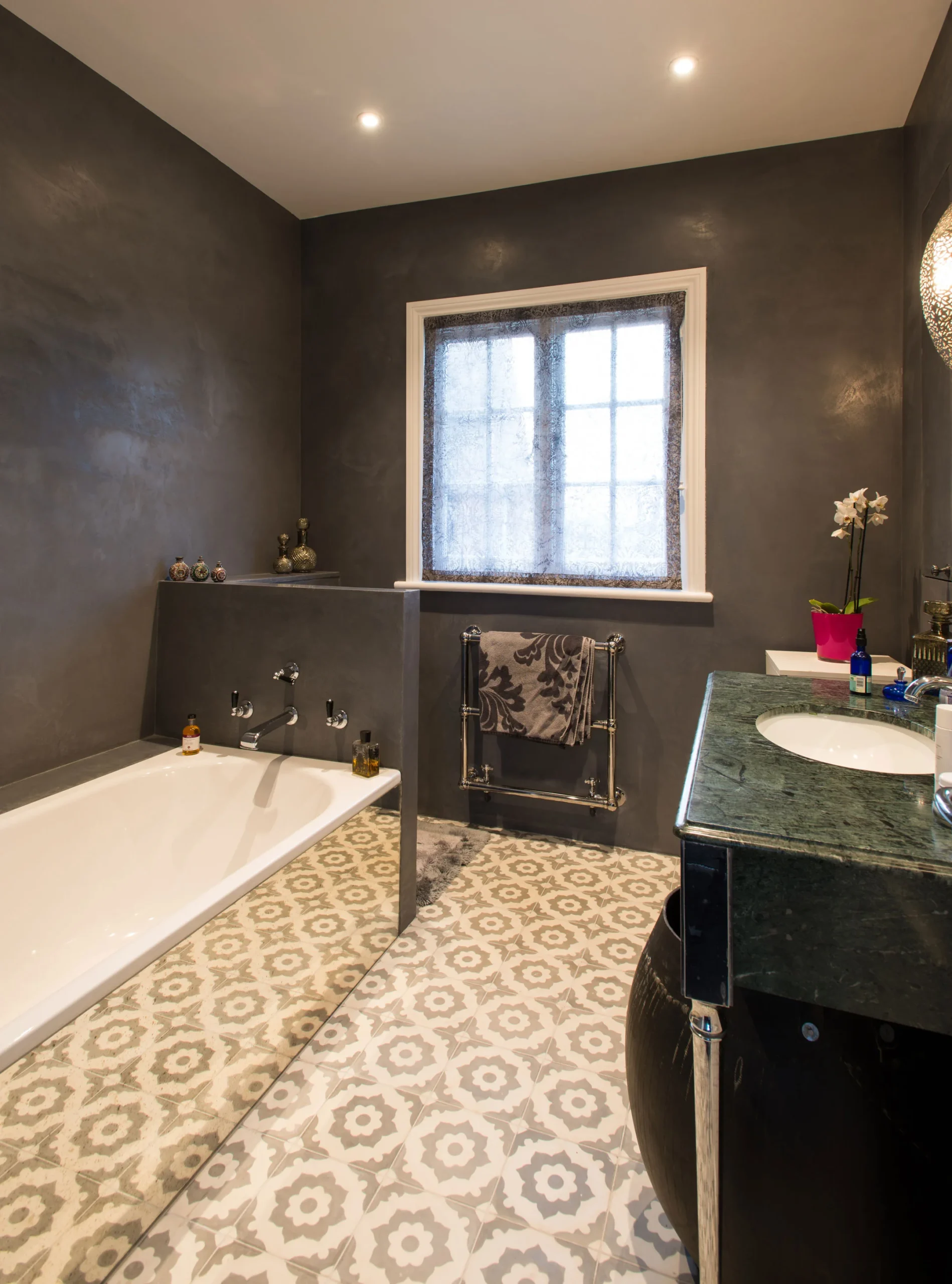 Bathroom with dark walls, patterned floor tiles, built-in bath and stone vanity