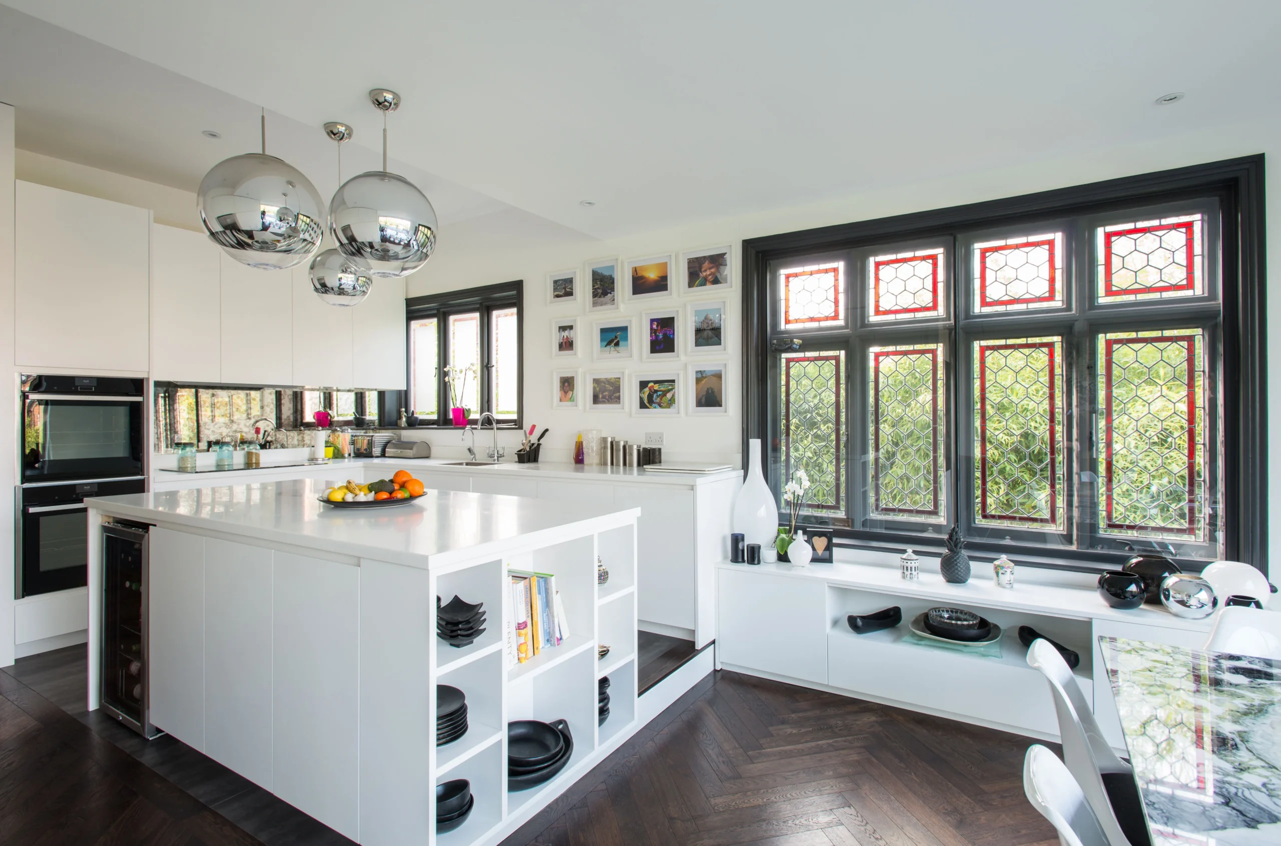 White handleless kitchen with open-shelved island, mirror pendants and original leaded stained glass windows