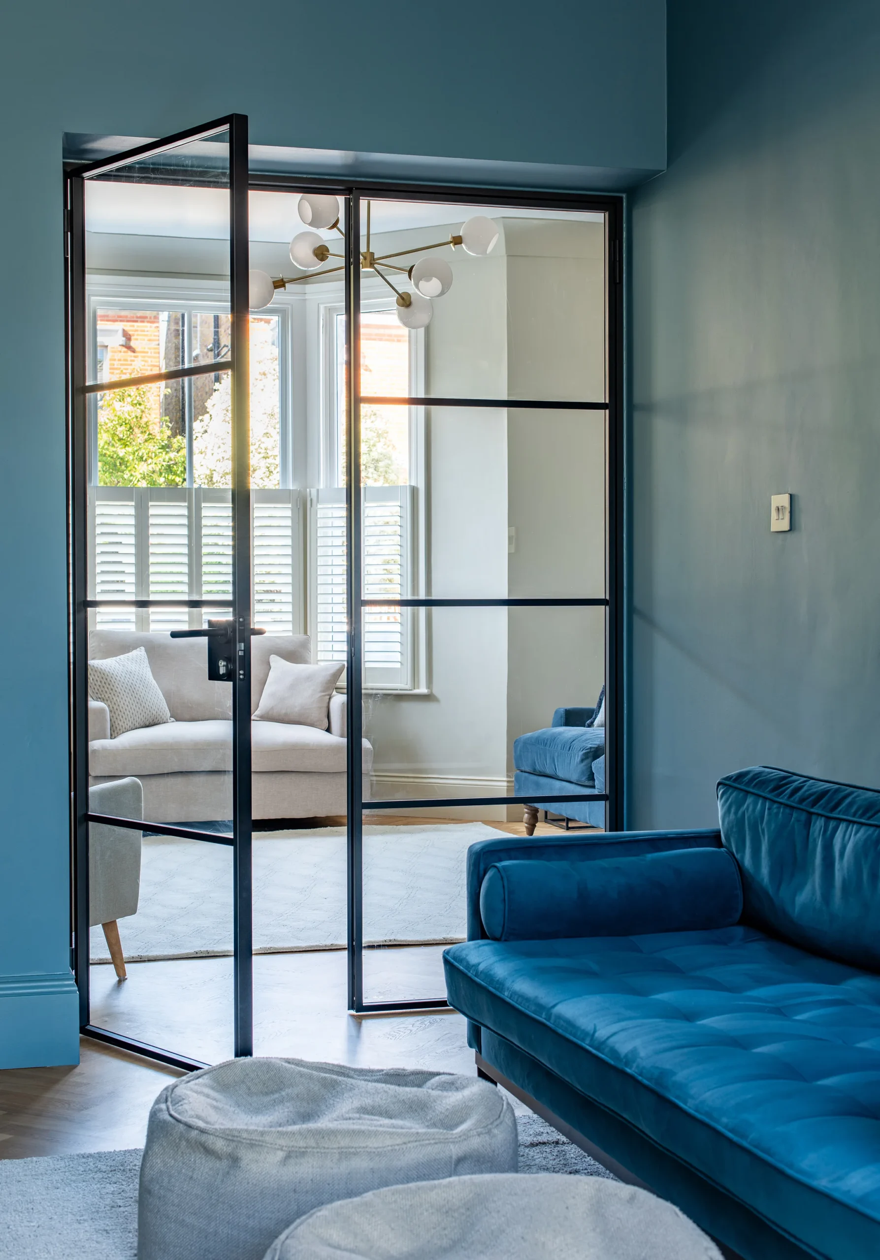 Teal snug with velvet sofa seen through a black steel glazed door