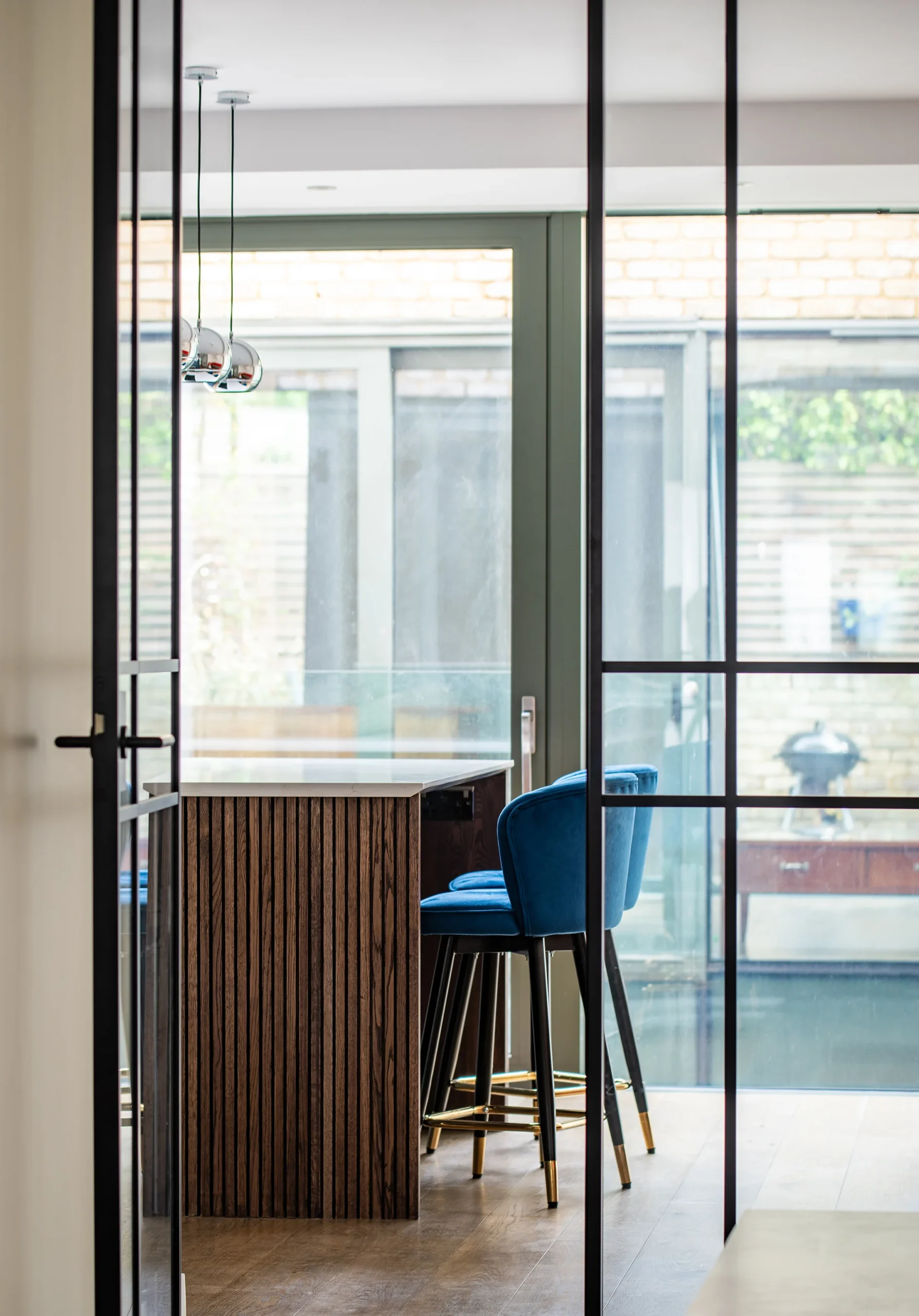 Hafer-Rd_2160px_3 Kitchen island with oak-slatted end and blue velvet stools seen through a black steel glazed door